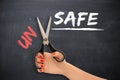 Woman transforming the word Ã¢â¬ÅunsafeÃ¢â¬Â into Ã¢â¬ÅsafeÃ¢â¬Â with scissors Royalty Free Stock Photo